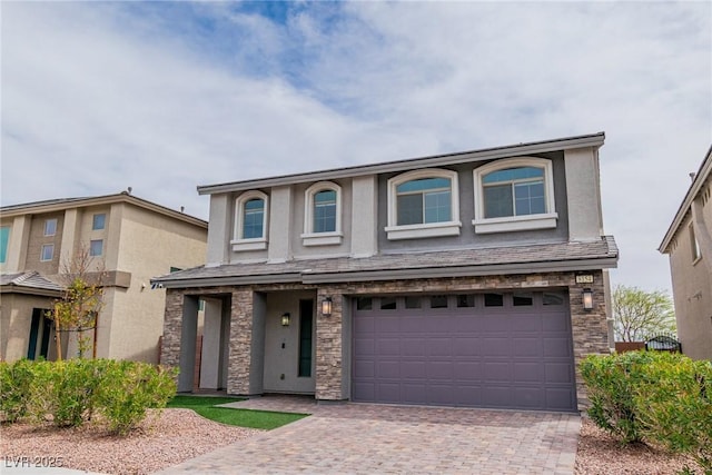 traditional-style home with decorative driveway, stone siding, a garage, and stucco siding