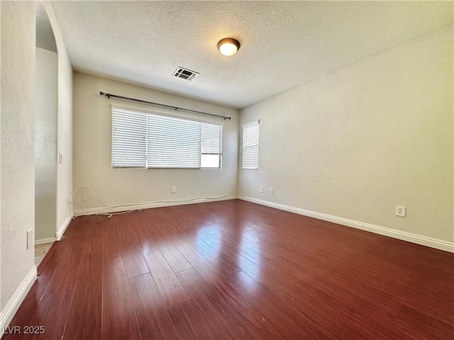 unfurnished room with dark wood-style flooring, baseboards, visible vents, and a textured ceiling