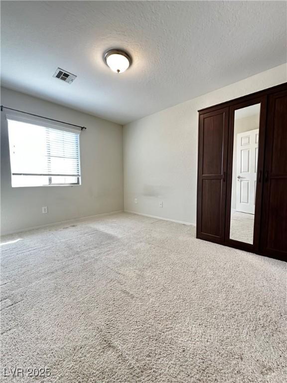 carpeted spare room with baseboards, a textured ceiling, and visible vents