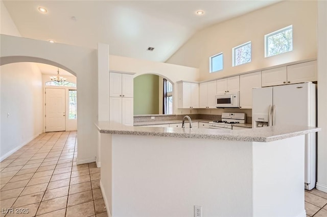 kitchen with a sink, white appliances, white cabinets, arched walkways, and light tile patterned floors