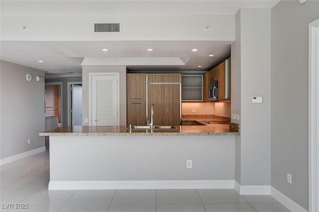 222 Karen Ave Unit 302, Las Vegas, NV 89109 - kitchen with stainless steel microwave, brown cabinets, a sink, visible vents, and light stone countertops