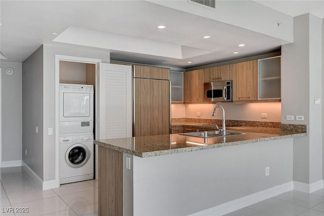 222 Karen Ave Unit 302, Las Vegas, NV 89109 - kitchen with stainless steel microwave, stacked washer / dryer, brown cabinetry, stone counters, and a sink