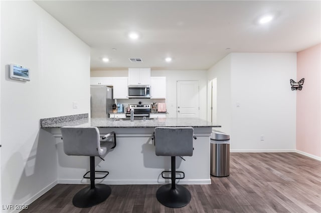 kitchen featuring white cabinets, appliances with stainless steel finishes, a kitchen breakfast bar, and dark wood finished floors