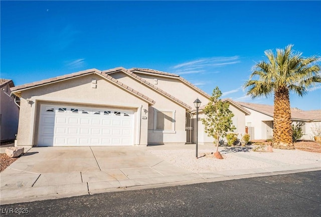 ranch-style house featuring concrete driveway, a tiled roof, a garage, and stucco siding
