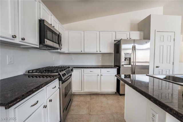 kitchen with white cabinetry, light tile patterned flooring, dark stone counters, lofted ceiling, and stainless steel appliances