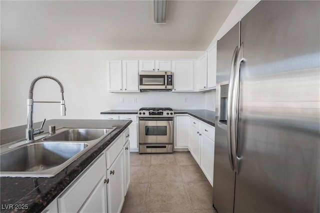 kitchen with light tile patterned floors, white cabinetry, appliances with stainless steel finishes, a sink, and dark countertops