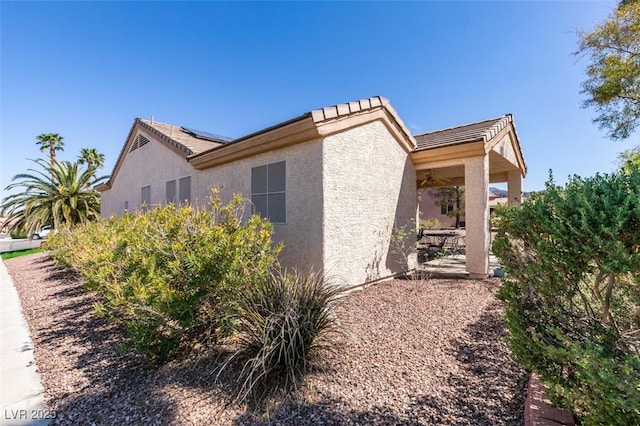 view of property exterior with stucco siding, solar panels, and a tile roof