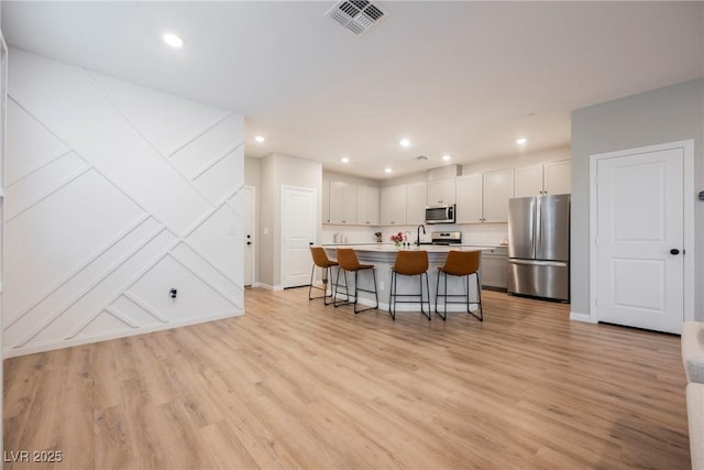3525 Serravalle Ln, Henderson, NV 89044 - kitchen with stainless steel appliances, a kitchen breakfast bar, light countertops, a center island with sink, and light wood-type flooring