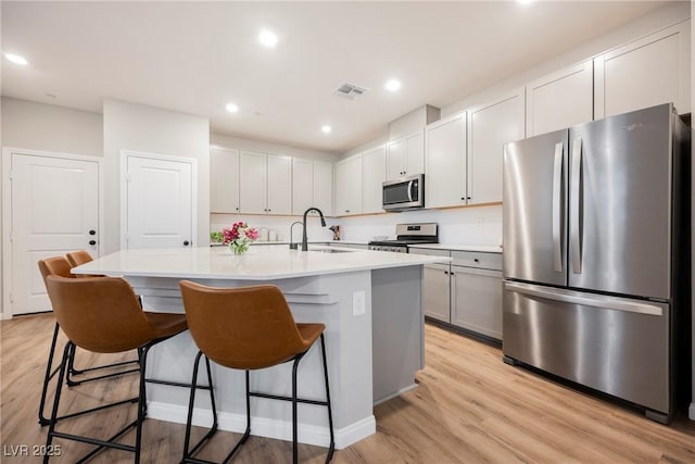 3525 Serravalle Ln, Henderson, NV 89044 - kitchen featuring appliances with stainless steel finishes, a sink, a breakfast bar, light wood-style flooring, and an island with sink