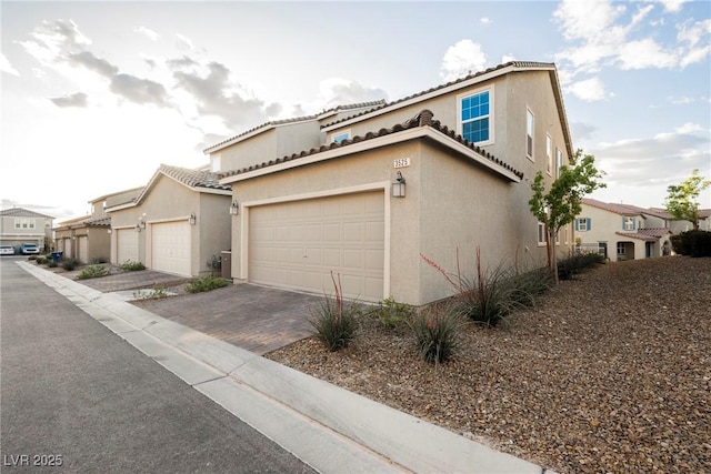 view of property exterior featuring a tiled roof, a garage, stucco siding, and decorative driveway