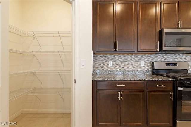 kitchen with dark stone counters, appliances with stainless steel finishes, dark brown cabinets, and backsplash