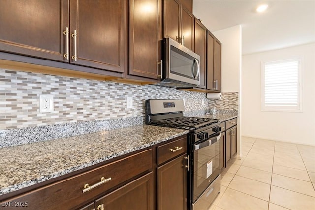 kitchen featuring light tile patterned floors, dark brown cabinets, light stone countertops, decorative backsplash, and stainless steel appliances