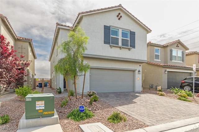 view of front facade featuring a garage, stucco siding, a tiled roof, and decorative driveway
