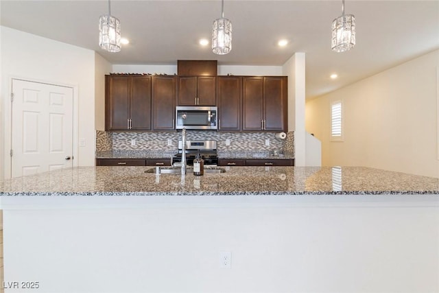 kitchen with tasteful backsplash, dark brown cabinetry, stainless steel microwave, stone counters, and pendant lighting