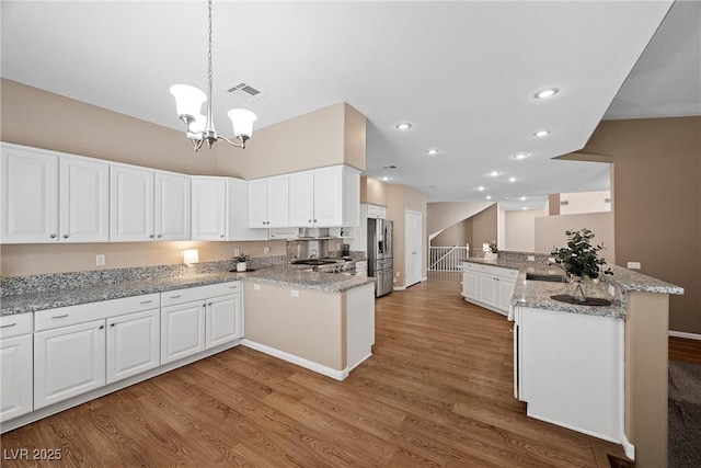 7460 Grassy Field Ct, Las Vegas, NV 89131 - kitchen featuring stainless steel refrigerator with ice dispenser, light wood finished floors, a chandelier, white cabinets, and decorative light fixtures