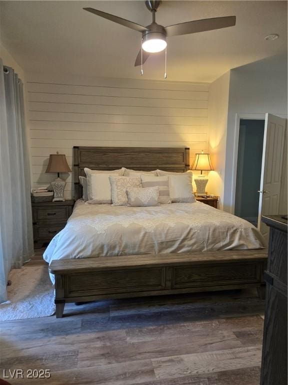 bedroom featuring wood finished floors, wooden walls, and a ceiling fan