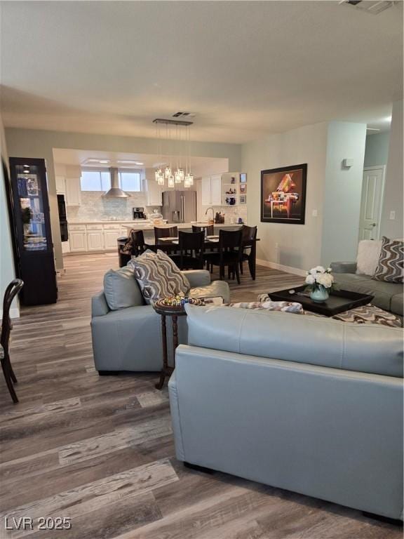 living room with visible vents, baseboards, an inviting chandelier, and wood finished floors
