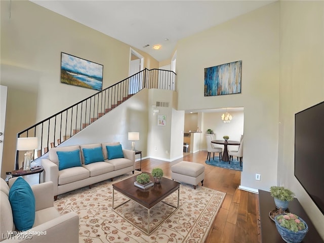 living room featuring stairway, a towering ceiling, visible vents, and wood finished floors