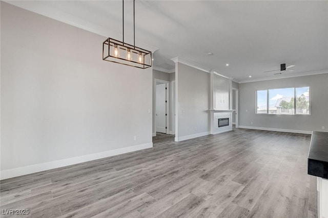 2110 S Manzanita Dr, Pahrump, NV 89048 - unfurnished living room with crown molding, ceiling fan with notable chandelier, light wood-style flooring, a glass covered fireplace, and baseboards