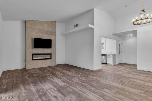 2851 S Valley View Blvd Unit 1098, Las Vegas, NV 89102 - unfurnished living room featuring wood finished floors, a chandelier, a tiled fireplace, baseboards, and vaulted ceiling