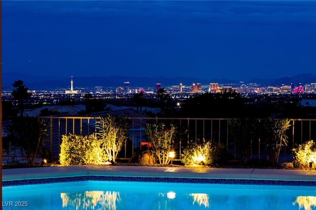 pool at twilight featuring a view of city lights, fence, and an outdoor pool
