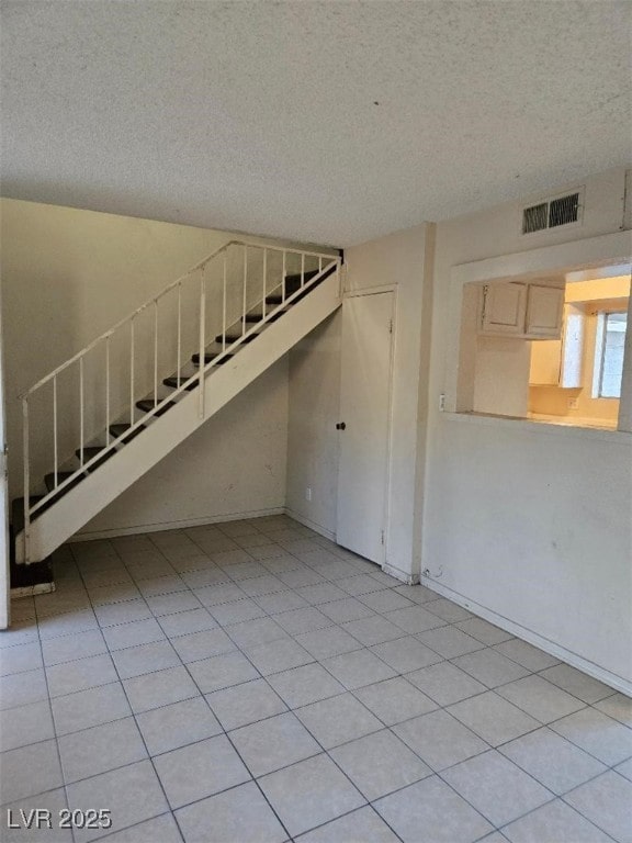 unfurnished living room featuring visible vents, baseboards, stairs, and a textured ceiling