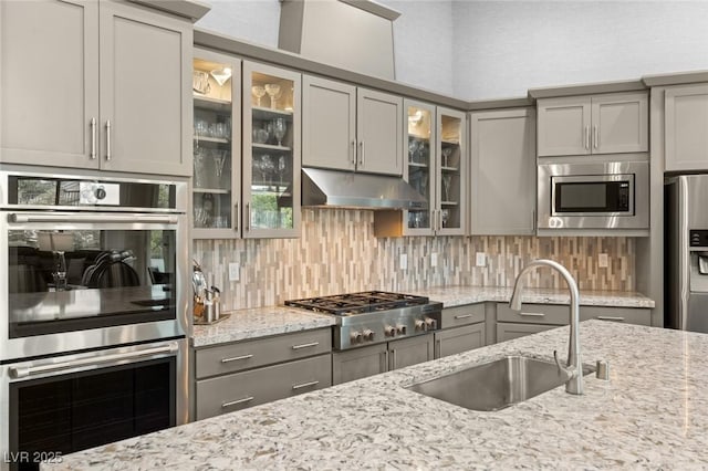 kitchen with tasteful backsplash, a sink, appliances with stainless steel finishes, under cabinet range hood, and gray cabinets