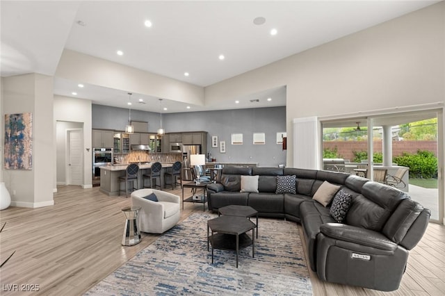 living area with recessed lighting, light wood-type flooring, a towering ceiling, and baseboards
