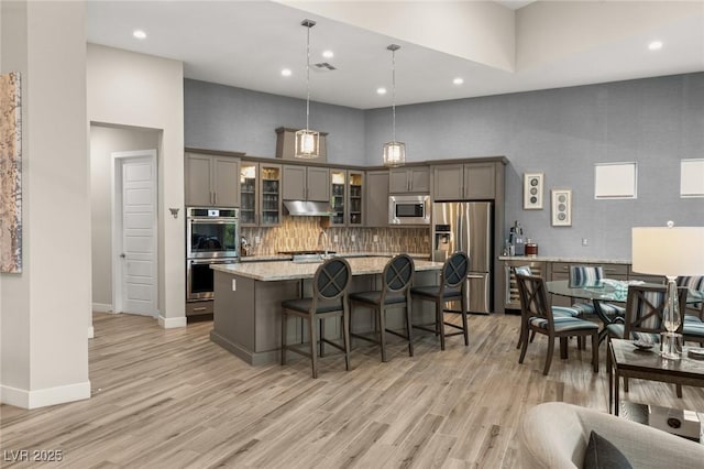 kitchen with stainless steel appliances, a center island with sink, visible vents, gray cabinetry, and under cabinet range hood