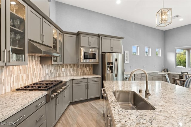 kitchen featuring stainless steel appliances, gray cabinetry, under cabinet range hood, and a sink