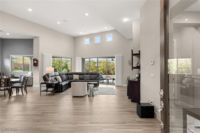 living room with light wood-style flooring, recessed lighting, a high ceiling, and baseboards