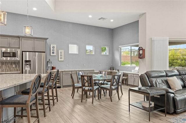 dining room with recessed lighting, light wood-type flooring, visible vents, and a high ceiling