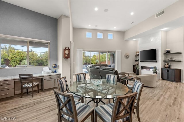 dining space featuring visible vents, a wealth of natural light, a high ceiling, and light wood-style floors