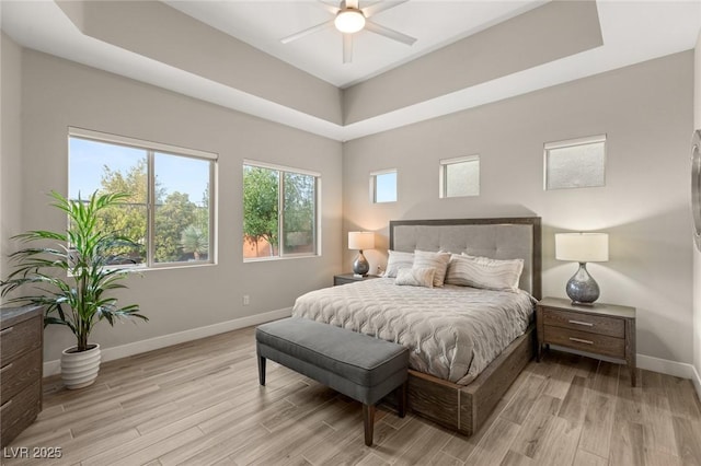 bedroom featuring light wood-style flooring, a raised ceiling, baseboards, and a ceiling fan