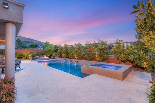 pool at dusk featuring a mountain view, a fenced backyard, a patio, an in ground hot tub, and a fenced in pool