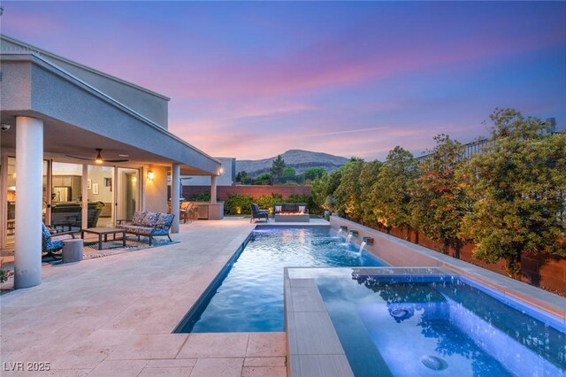 pool at dusk with a mountain view, an outdoor living space, a patio area, and an in ground hot tub