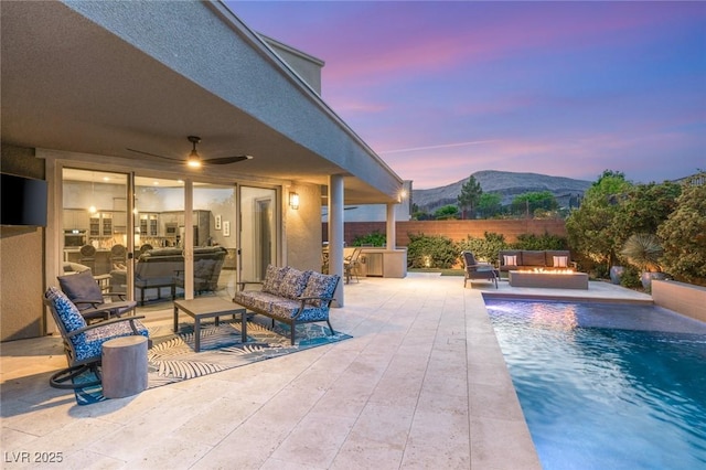 pool at dusk featuring a mountain view, an outdoor living space with a fire pit, a patio, and a fenced in pool