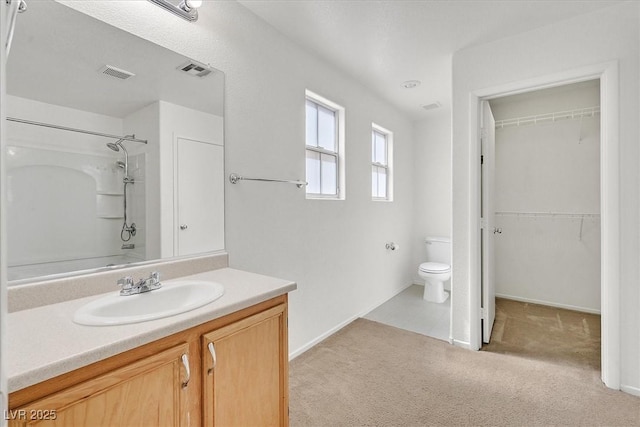 bathroom with a shower, vanity, toilet, baseboards, and a spacious closet