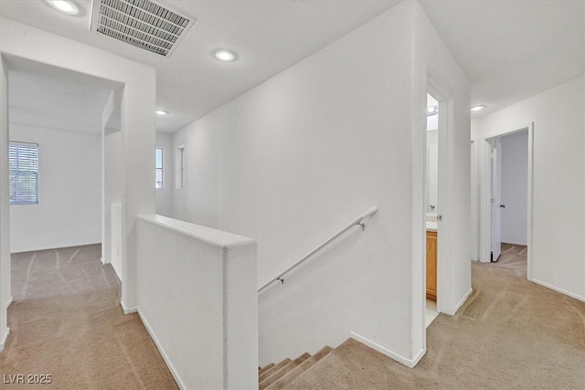 hall with an upstairs landing, light carpet, recessed lighting, and baseboards