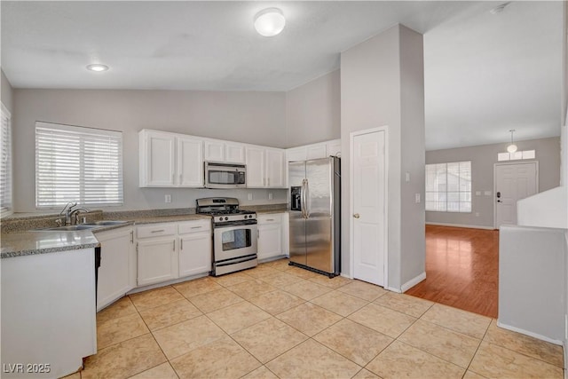 kitchen with a sink, light tile patterned floors, stainless steel appliances, baseboards, and white cabinetry