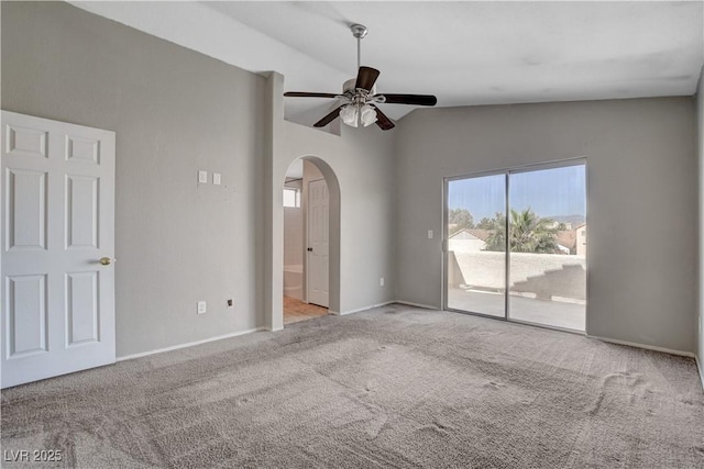 carpeted empty room featuring arched walkways, a ceiling fan, vaulted ceiling, and baseboards