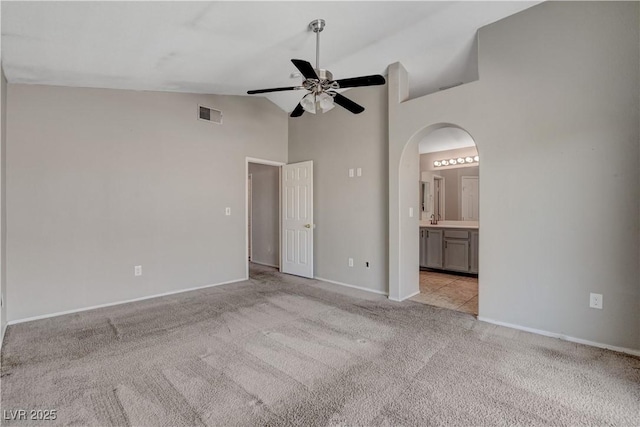 unfurnished bedroom featuring visible vents, light colored carpet, connected bathroom, baseboards, and high vaulted ceiling