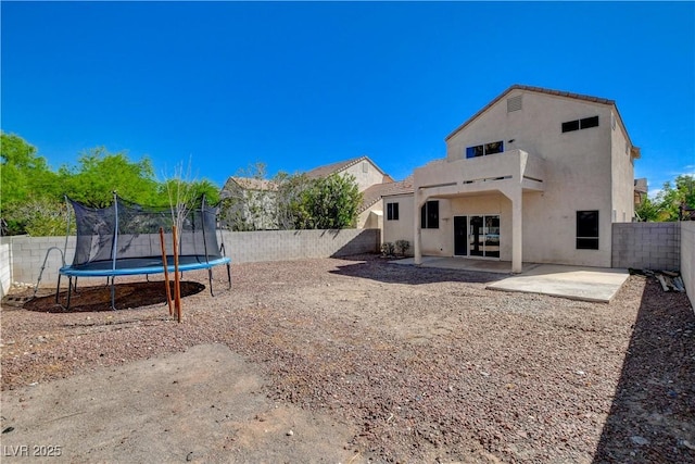 rear view of property featuring stucco siding, a fenced backyard, a patio, and a trampoline
