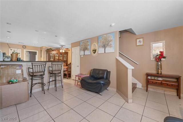living area with light tile patterned floors, baseboards, a ceiling fan, and stairs