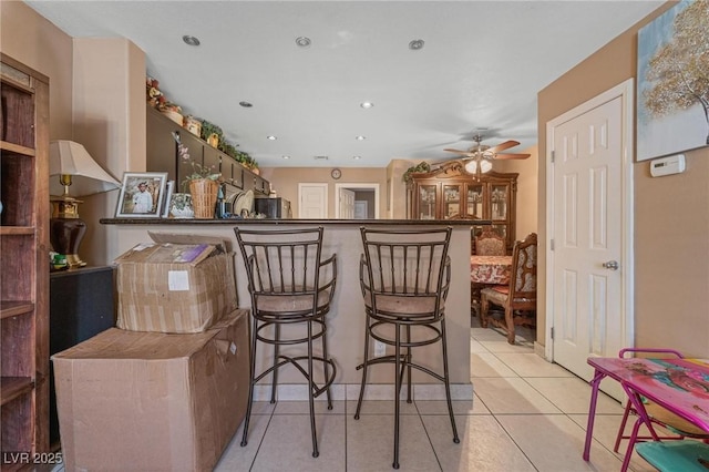 interior space with a breakfast bar, recessed lighting, light tile patterned flooring, ceiling fan, and fridge