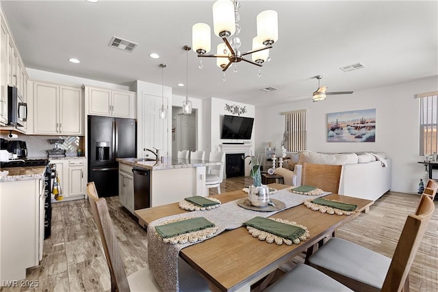 10052 Silver Comet Ct, Las Vegas, NV 89178 - dining room featuring light wood-type flooring, a chandelier, a fireplace, a ceiling fan, and recessed lighting