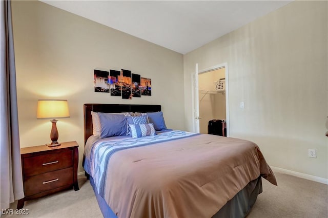 bedroom with light carpet, a walk in closet, and baseboards