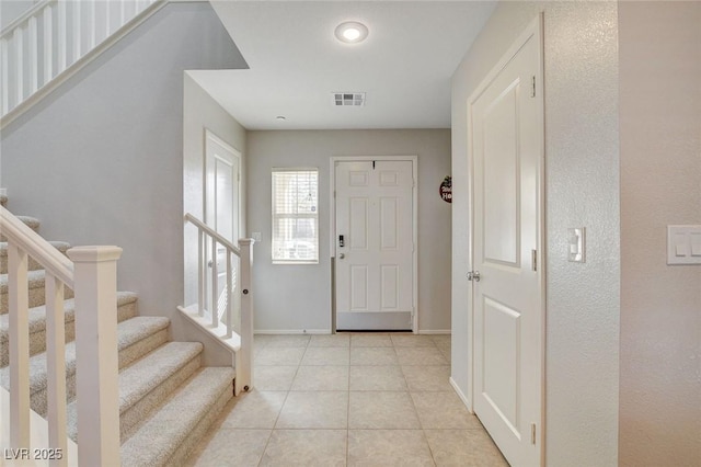 foyer entrance with visible vents, baseboards, stairway, and light tile patterned floors