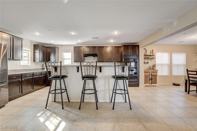 kitchen with a breakfast bar area, dobule oven black, freestanding refrigerator, and dark brown cabinets