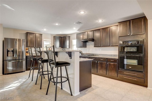 kitchen with visible vents, a kitchen bar, dark brown cabinets, stainless steel appliances, and light stone counters